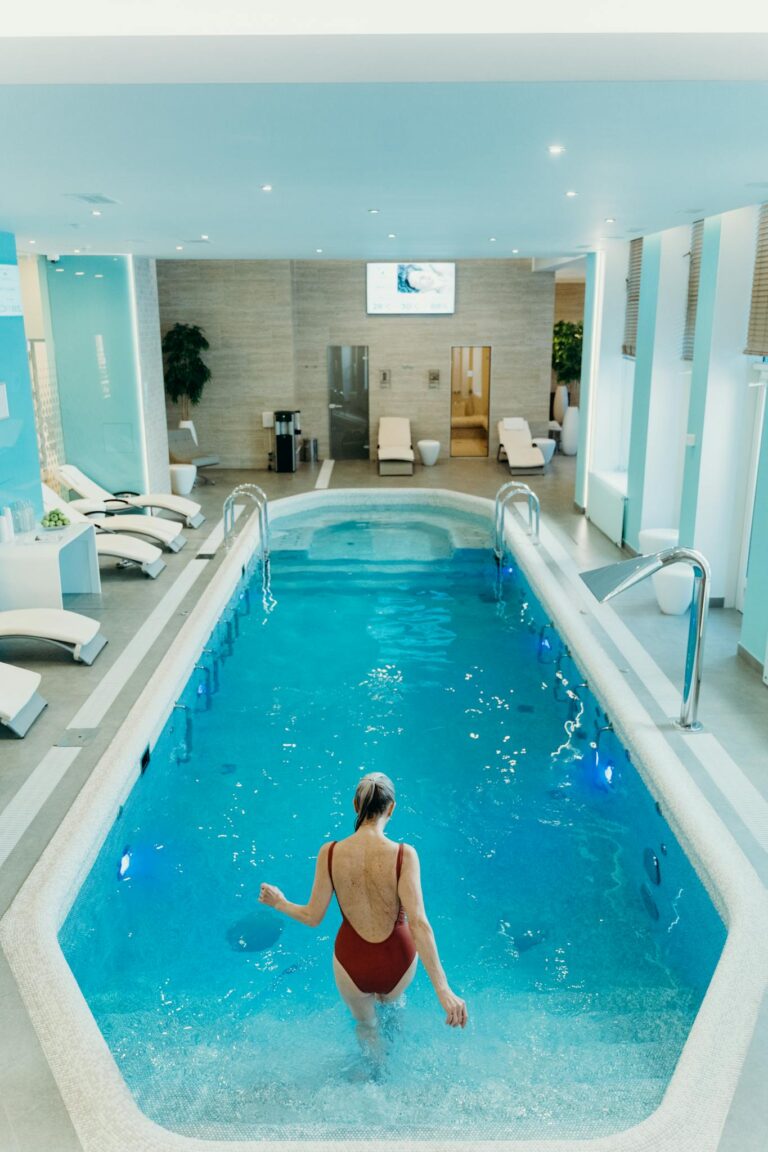 A serene indoor swimming pool setting with a woman in a red swimsuit stepping in.